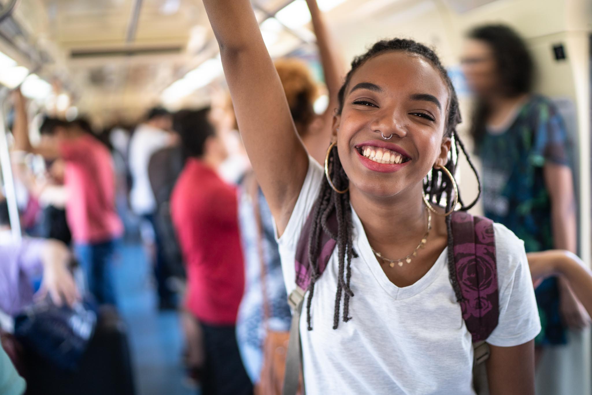 Passageira em pé dentro de um vagão de metrô movimentado, segurando no apoio superior.